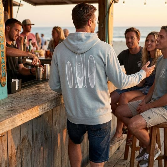 man at a beach bar wearing a surfboard sweatshirt with his friends on the beach
